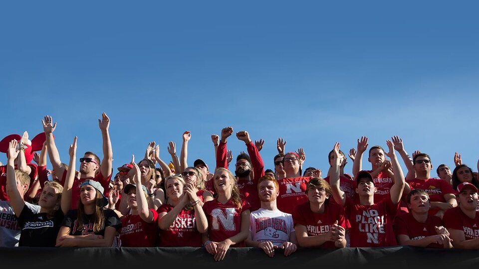 Students cheering at football game with blue sky behind them